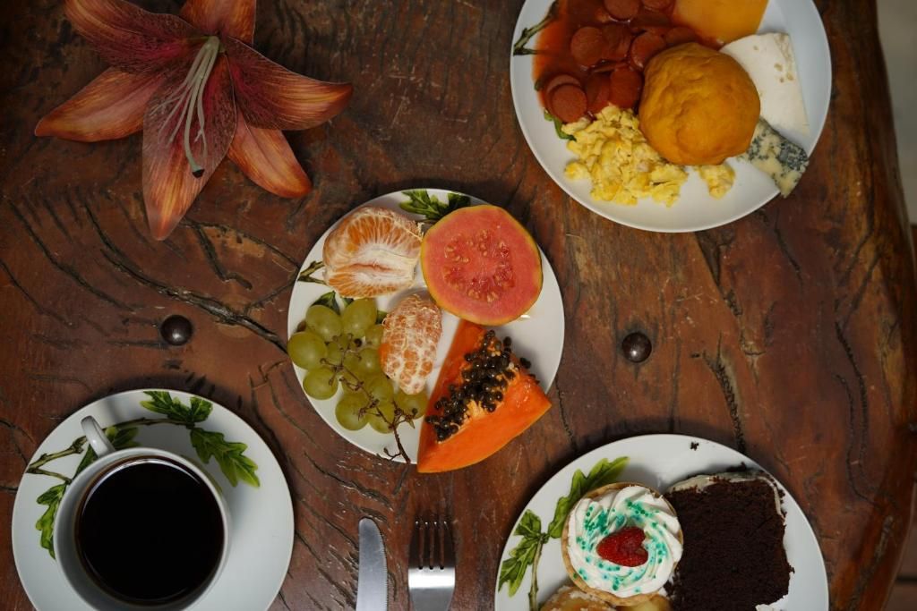 Pratos do café vistos de cima: frutas, ovos, pão de queijo, bolo e café